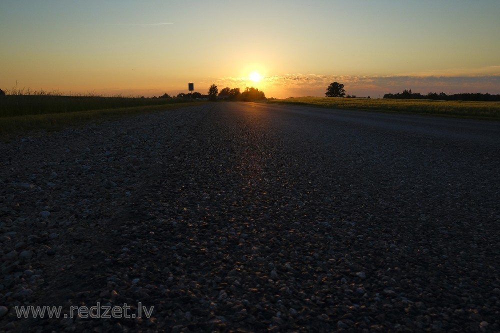 Saulrieta ainava, asfalta ceļa tuvplāns