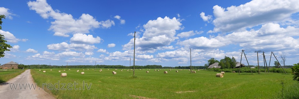 Lauku panorāma ar siena ruļļiem un mākoņainām debesīm