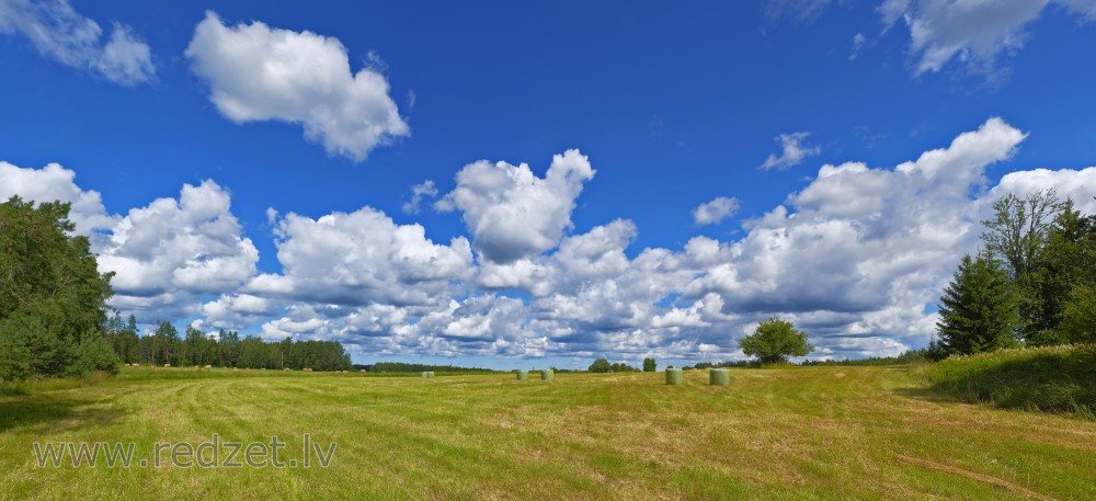 Lauku panorāma ar siena ruļļiem un mākoņainām debesīm