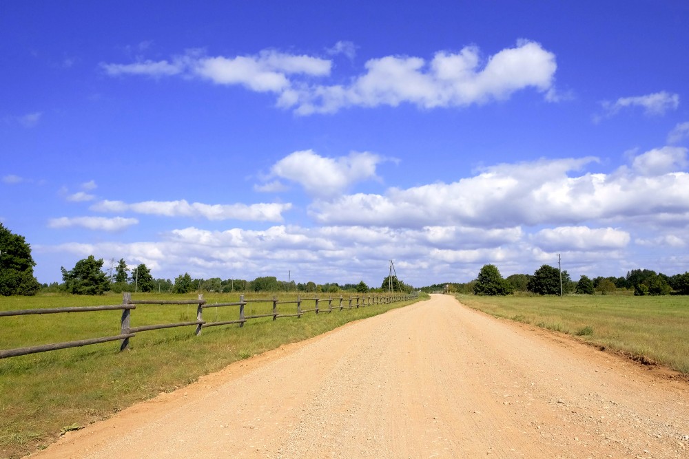 Gravel country road with wooden fence and cloudy sky