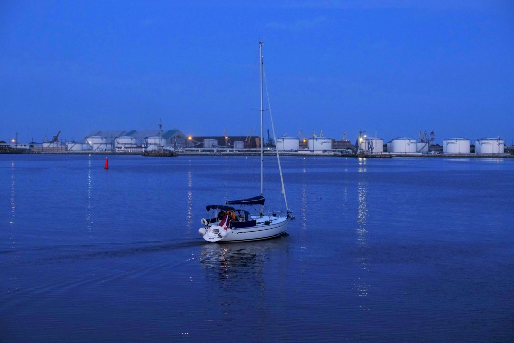 Yacht on the Venta River with the port of Ventspils in the evening
