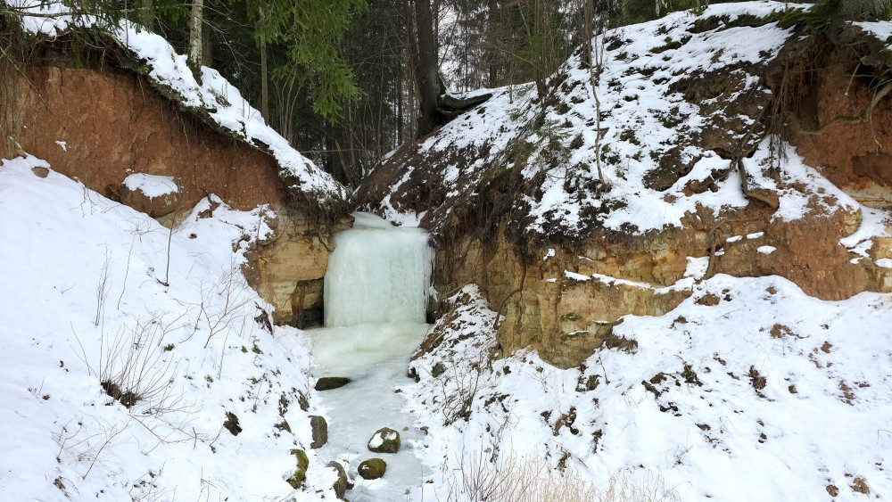 Aizsalis ūdenskritums Omiķu gravā starp sniegotām nogāzēm
