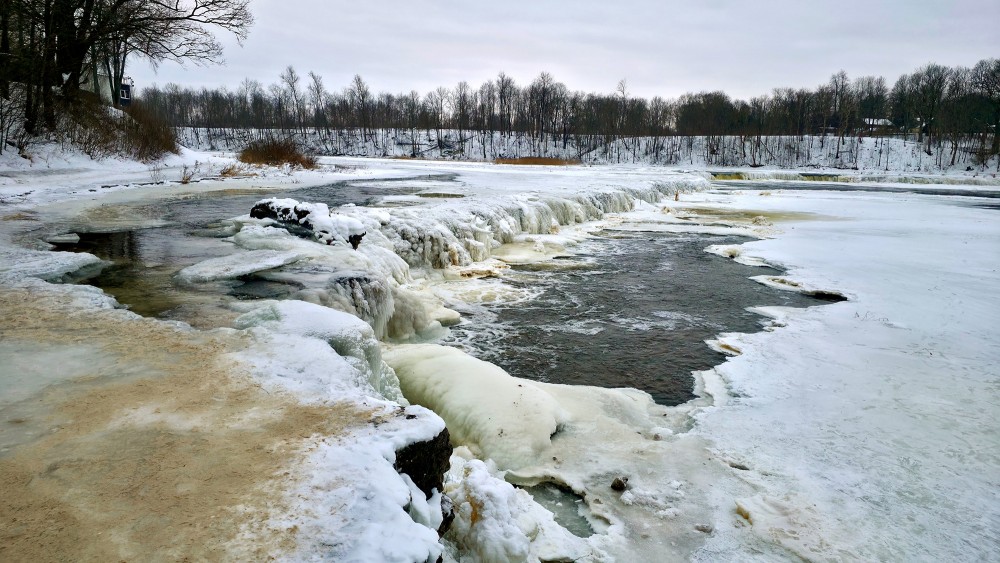 Frozen Venta waterfall in winter with ice formations and open river flow