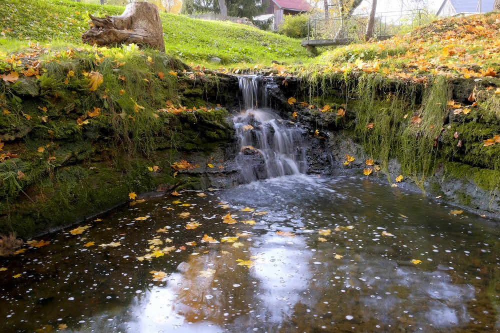 Rumbiņas ūdenskritums rudenī ar kritušām lapām un sūnainu nogāzi