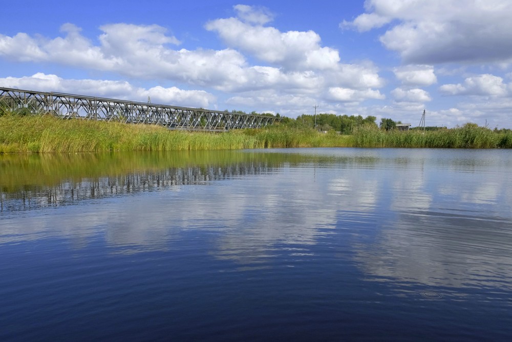 Metāla tilts pār Papes kanālu mierīgā piekrastes ainavā