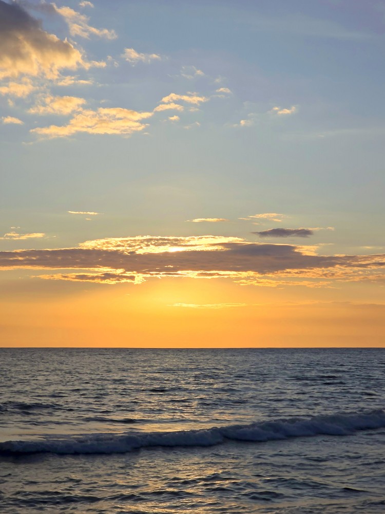 Zeltains saulriets virs mierīgas jūras ar mākoņiem un viļņiem