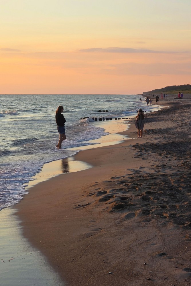 Evening walk on the beach during sunset with wooden pier in the sea Evening walk on the beach during sunset with wooden pier in the sea