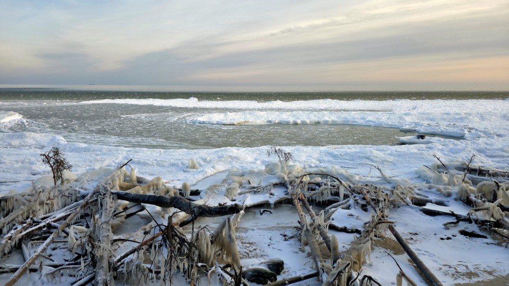 Kolkasraga ziemas piekraste ar apledojušiem sanesumiem un jūras ledu pie horizonta