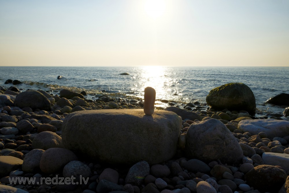 Akmeņu kompozīcija jūrmalā saulrieta gaismā