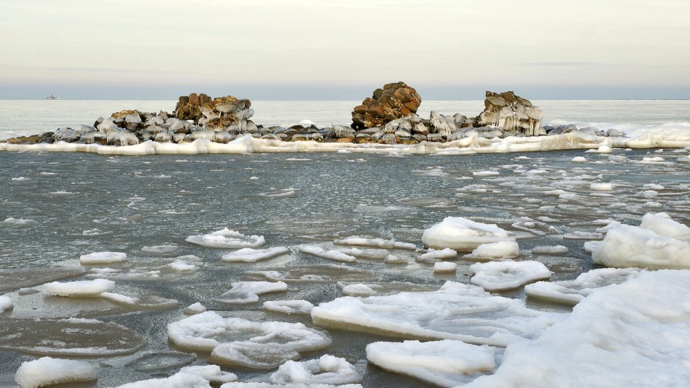 Old Kolkasrags lighthouse and drifting ice on the winter sea near the horizon