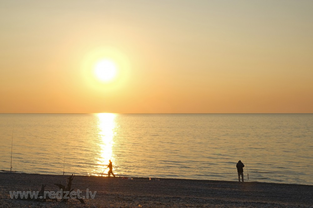 Makšķernieku silueti saulrietā