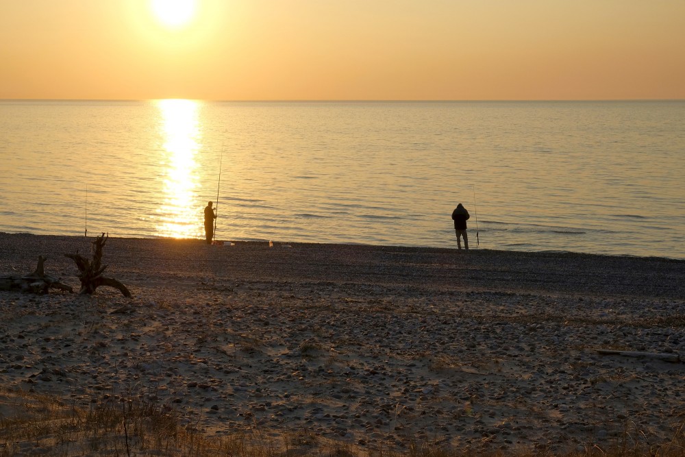 Makšķernieki saulrietā jūras krastā