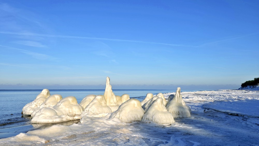 Ice-covered pier on Staldzene coast with snowy shoreline in winter