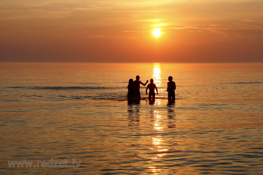 Cilvēku silueti jūrā, saulrietā