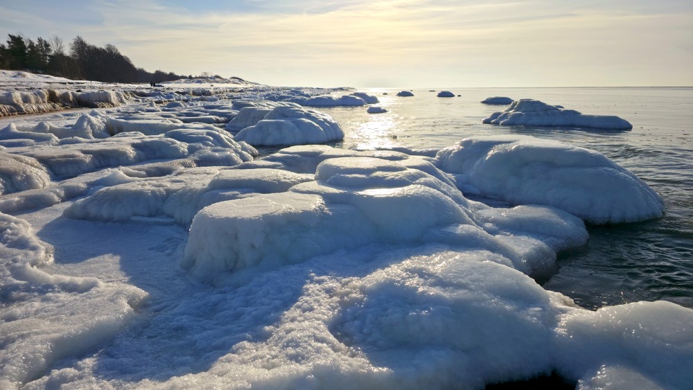 Saules apspīdēti apledojuši akmeņi Užavas jūrmalā saulrietā