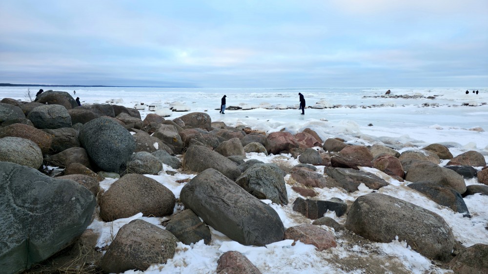 Icy rocks and people walking on the frozen Mērsrags coastline