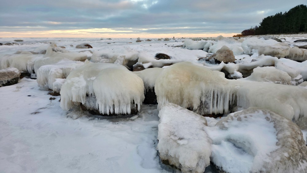 Icy boulders with icicles on the Mērsrags coast at sunset
