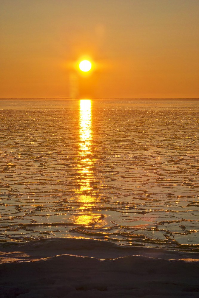 Vertikāla saulrieta ainava ar zeltainu gaismas ceļu uz ledus