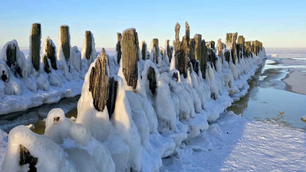 Frozen wooden breakwaters in sunlight at Bigauņciems