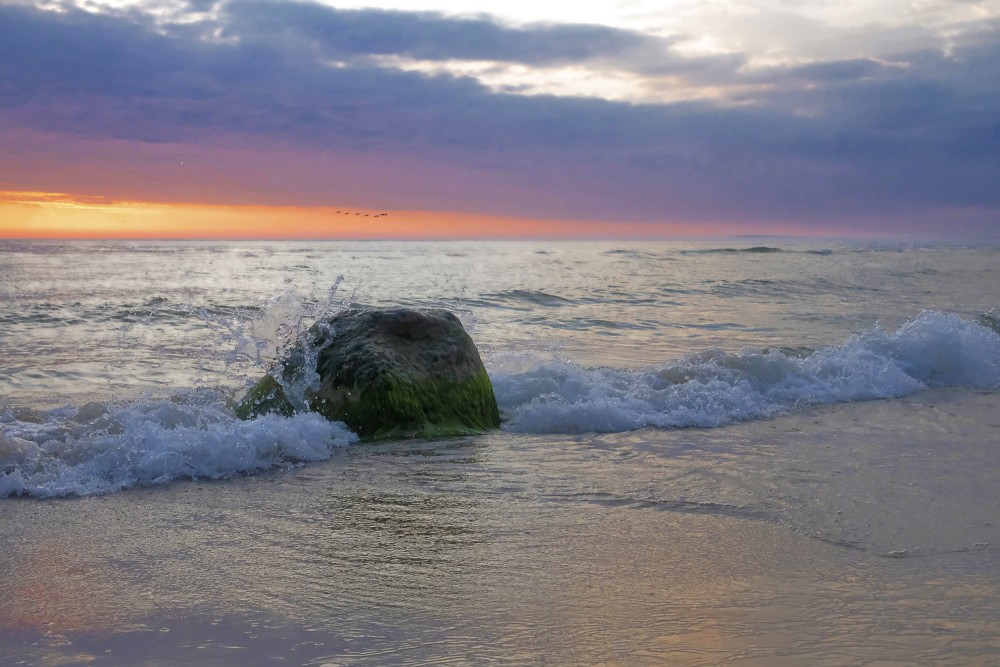 Jūra, akmens un viļņu šļakatas saulrietā