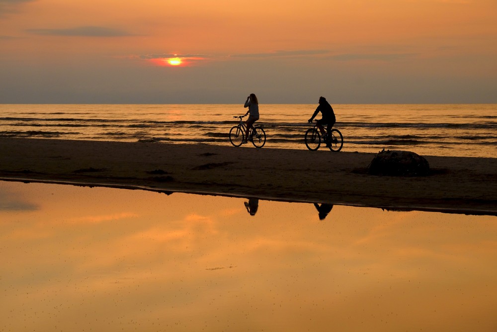 Riteņbraucēji saulrietā pludmalē Riteņbraucēji saulrietā pludmalē