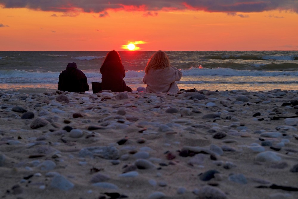 Sēdoši cilvēki pie jūras saulrietā