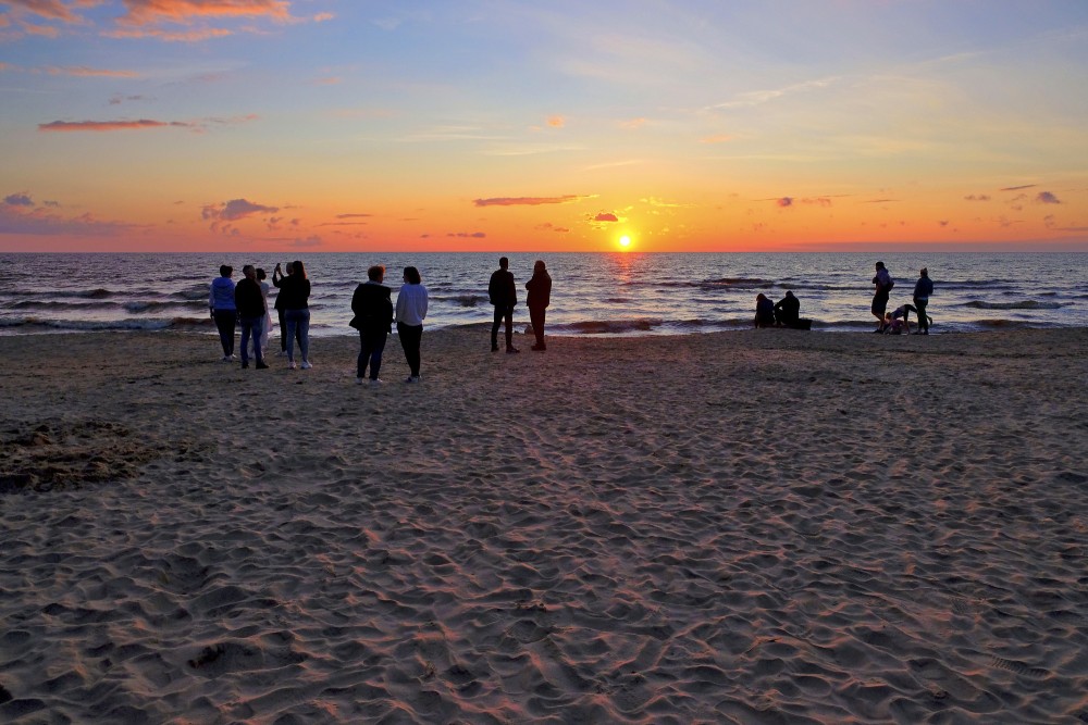 Cilvēki vēro saulrietu jūrā