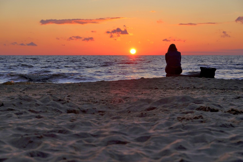 Sēdoša cilvēka siluets saulrietā