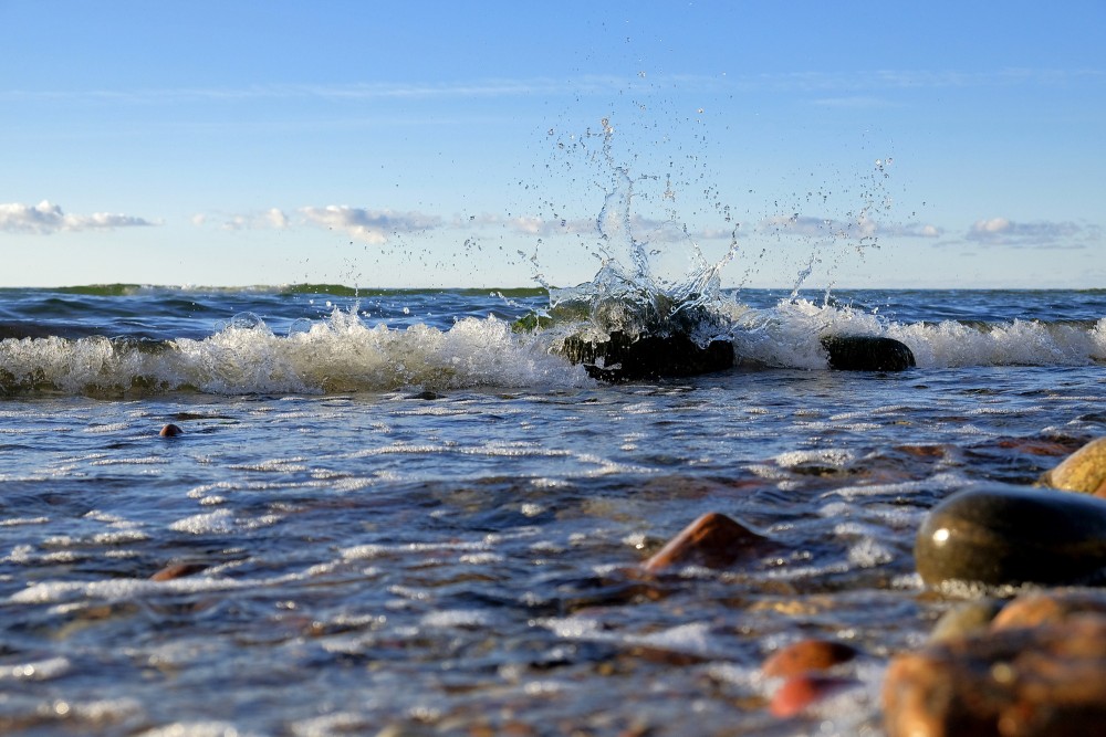 Jūras viļņa šļakatas pret akmeni saulainā piekrastē