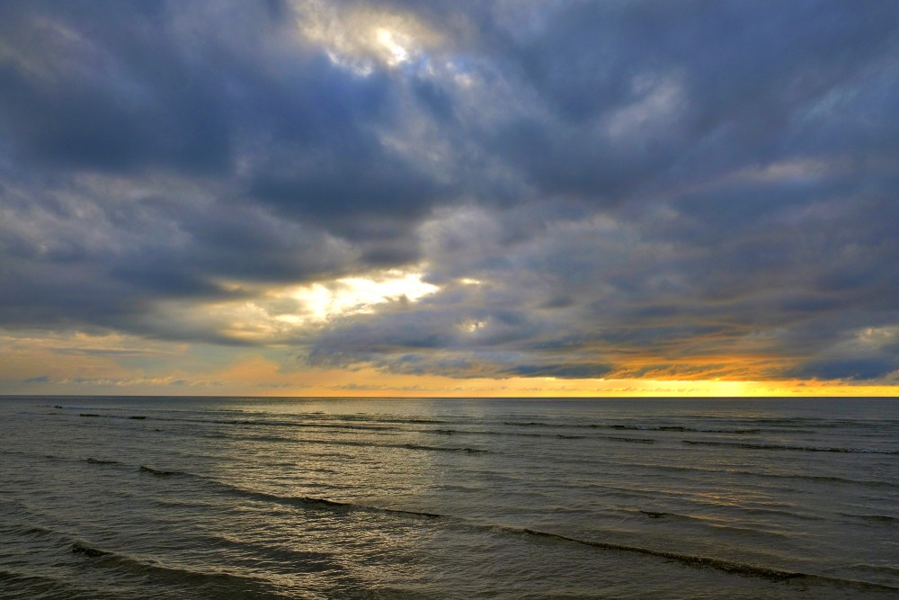 Drūmām mākoņiem klāts jūras skats ar saulrieta gaismas joslu