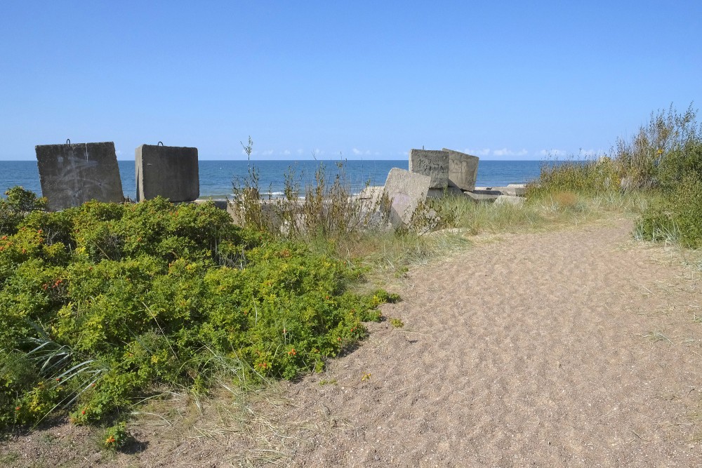 Smilšains ceļš gar piekrasti ar betona blokiem pie jūras