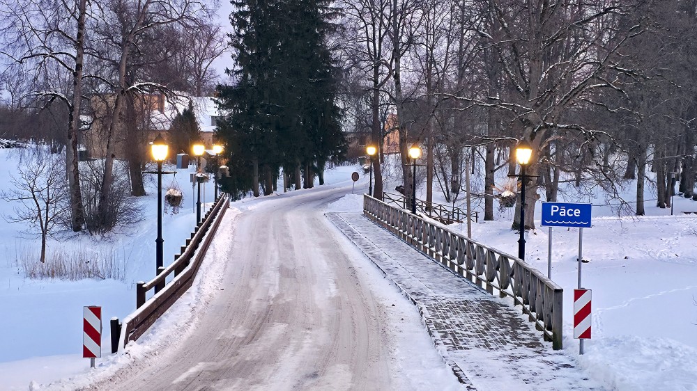 Tilts pār Pāces upi ziemā ar sniegotu ceļu un laternām Tilts pār Pāces upi ziemā ar sniegotu ceļu un laternām
