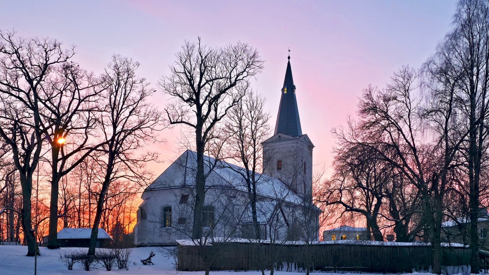 Dundagas luterāņu baznīca ziemas saulrietā ar sniegu un kailiem kokiem