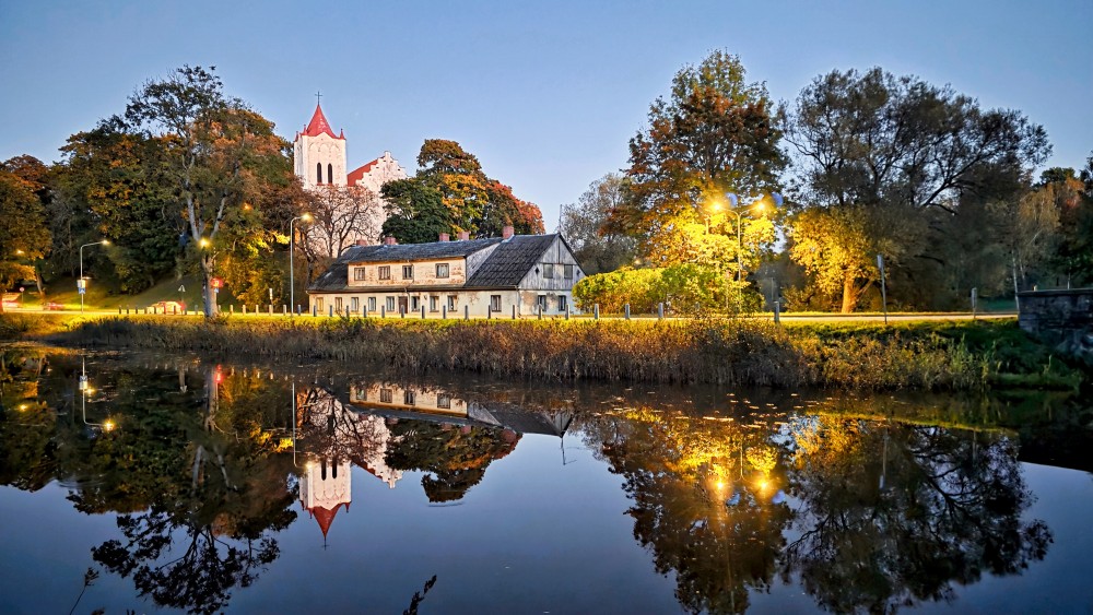 Aizpute St John Lutheran Church and building reflecting in water at night