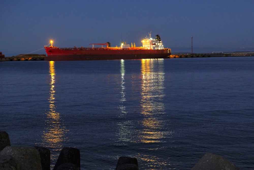 Kravas kuģis ostā vakara stundā ar gaismu atspulgiem ūdenī