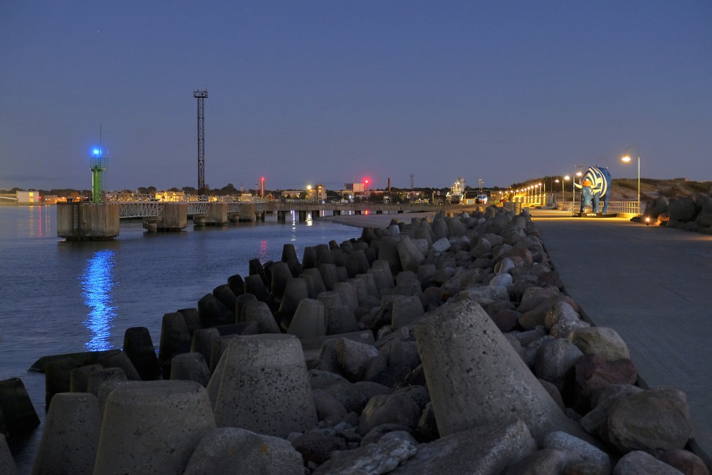 Ventspils Dienvidu mola promenāde krēslā ar ostu un skulptūru Govs Matrozis