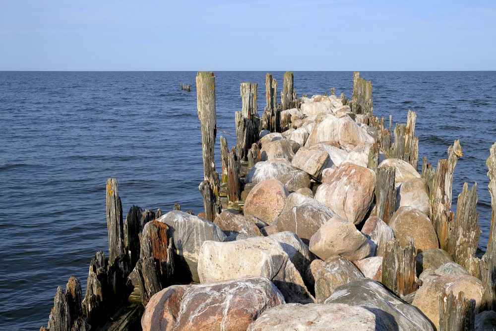 Akmens mols ar vertikāliem koka pāļiem jūrā