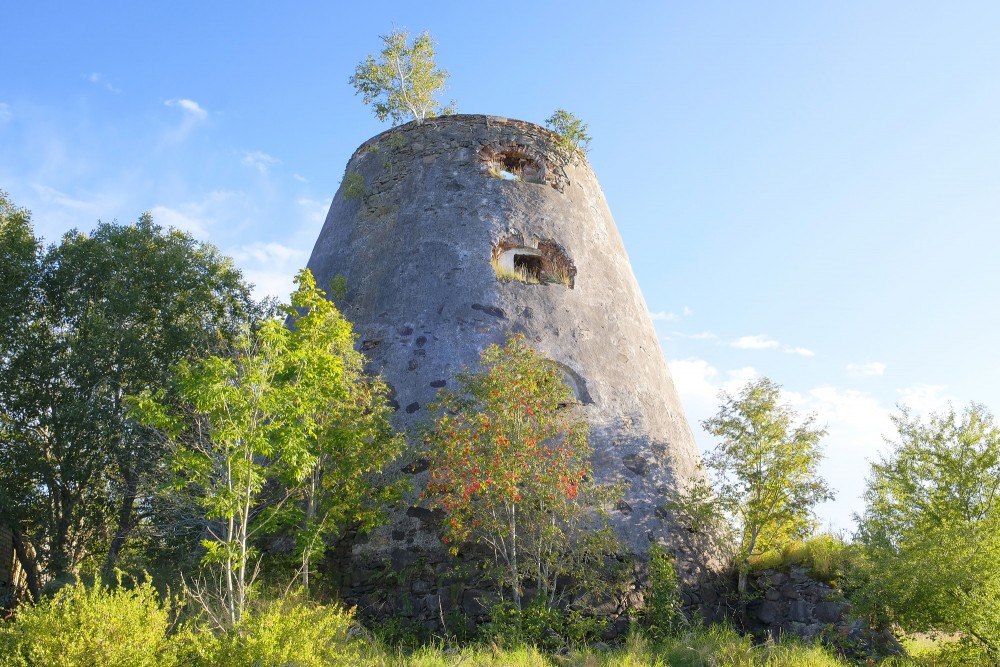 The conical masonry ruins of Minde windmill behind green trees