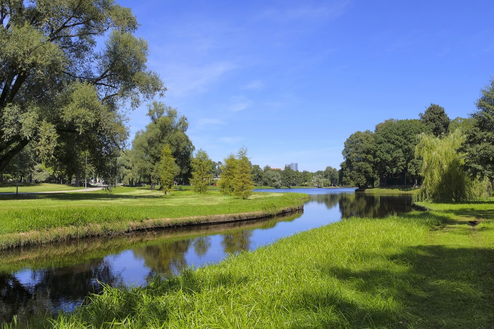 Zaļā zona pie Māras dīķa ar mierīgu kanālu un plašu parka ainavu