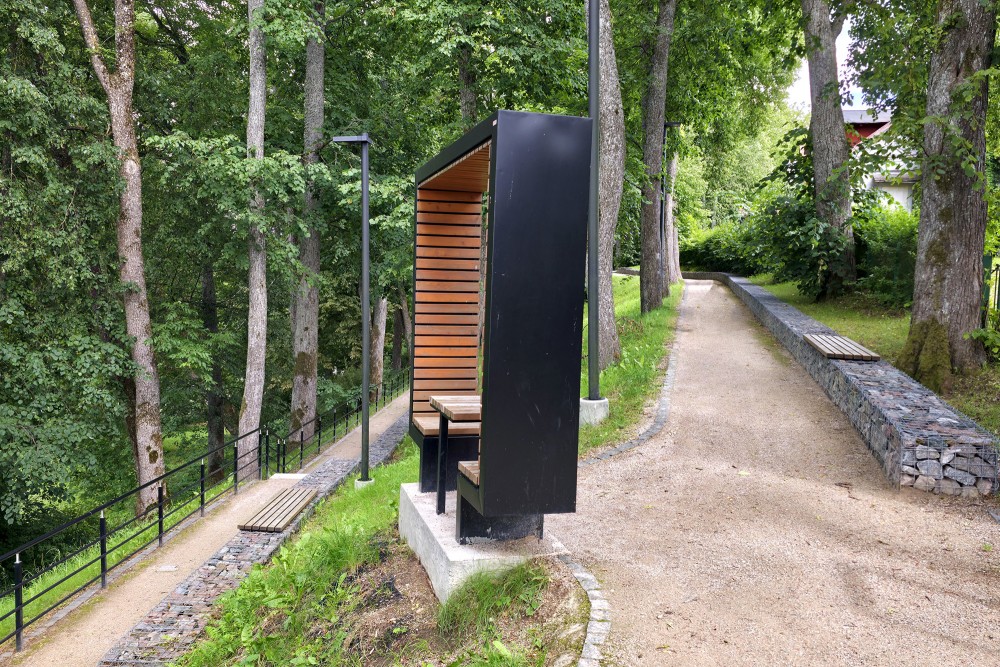 Stylized Frame "Framing Talsi" Beside a Tree-Lined Path and Gabion Wall