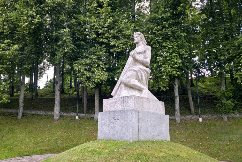 Monument "Koklētājs" in Talsi against a backdrop of lush green trees Monument "Koklētājs" in Talsi against a backdrop of lush green trees