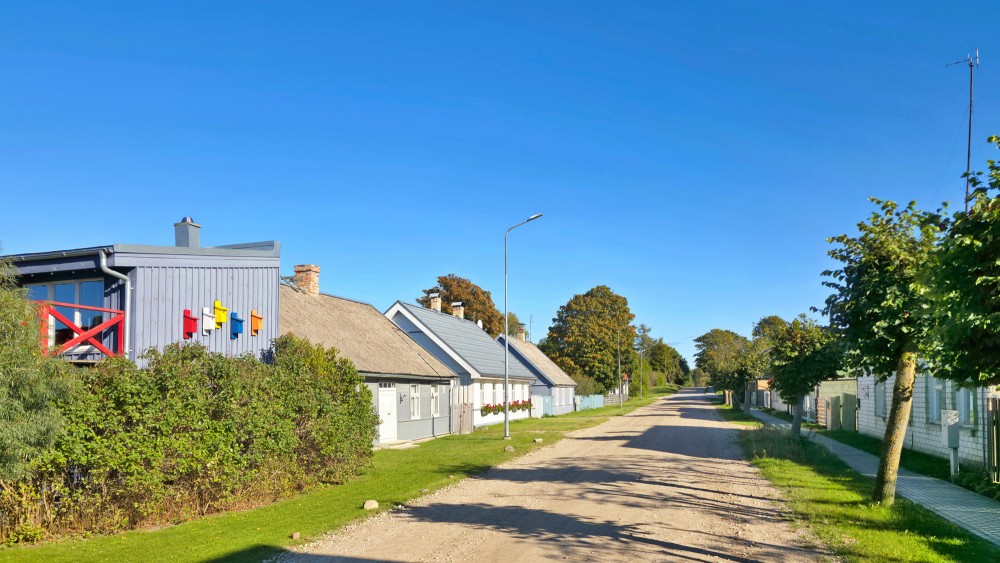 Mājīga Pāvilostas iela ar koka ēkām un krāsainām putnu būrīšu dekorācijām