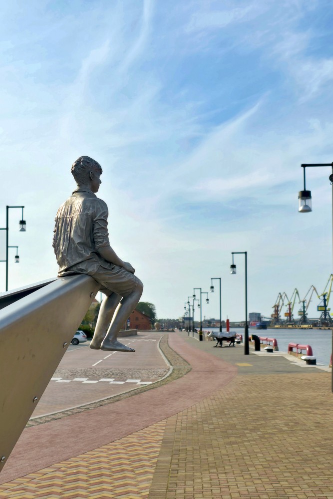 Boy sculpture on steel boat at Ventspils port waterfront