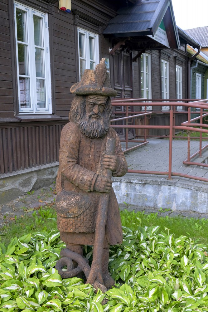 Koka skulptūra ar bārdainu vīru pie vēsturiskas ēkas Plateliai pilsētā