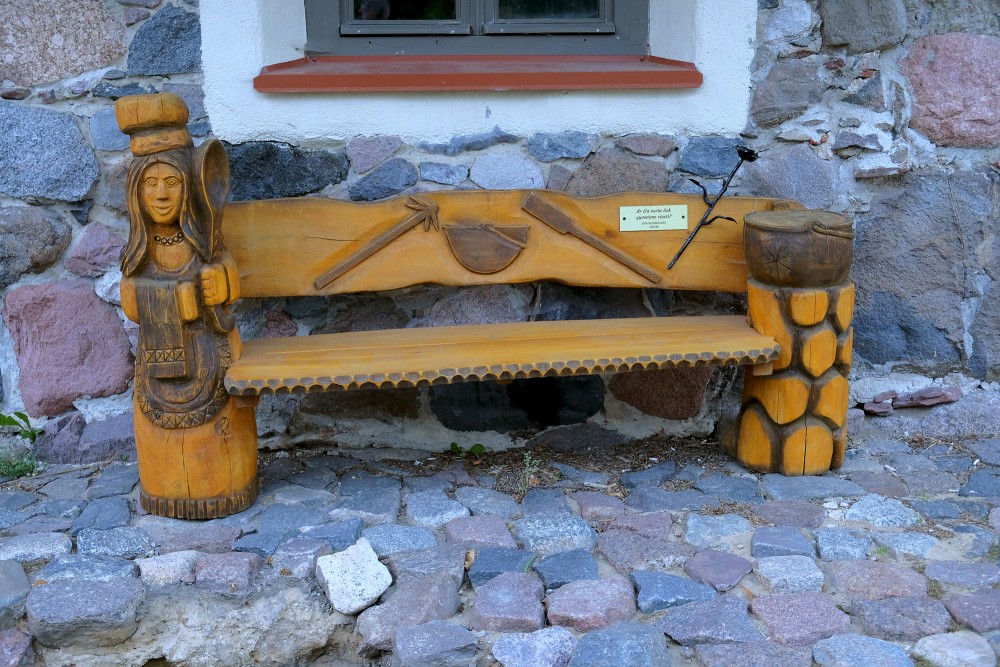 Kokgriezuma soliņš pie Sedas ūdensdzirnavu akmens sienas ar dekoratīvu figūru