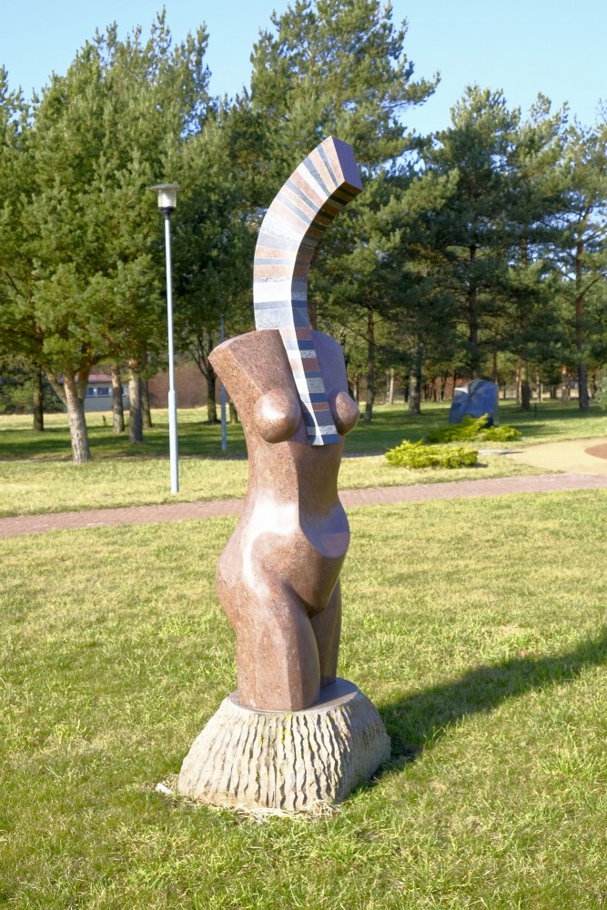 Abstrakta akmens skulptūra cilvēka torsā zālienā pie parka celiņa