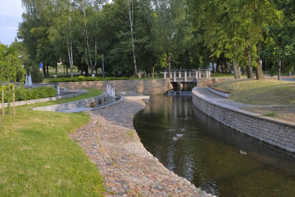 A scenic bend of the canal with a small bridge and fountains in Marijampole Poetry Park
