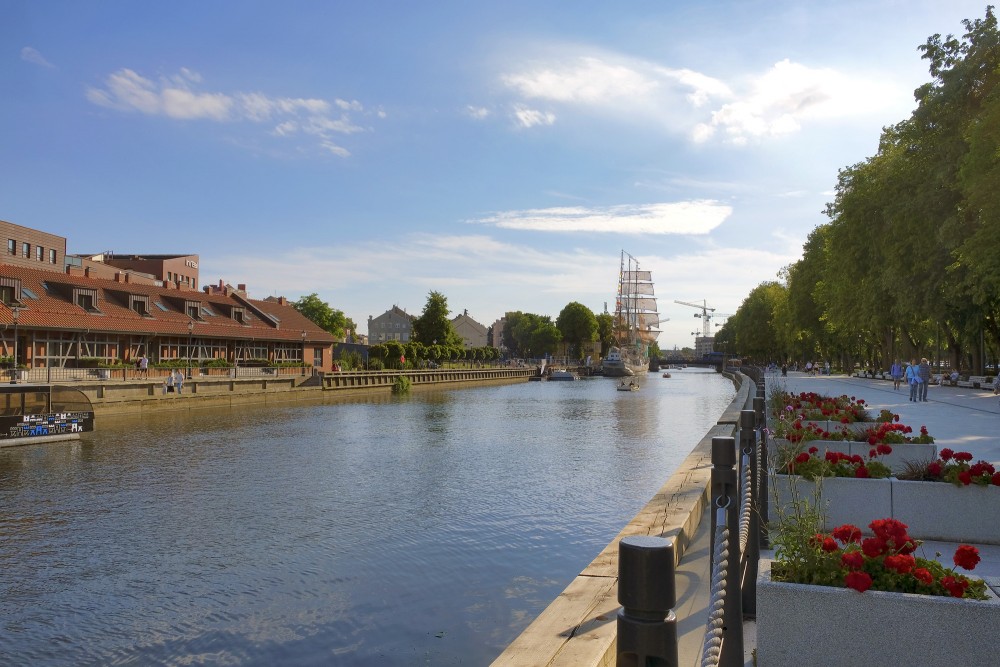 Danes river promenade in Klaipeda with red geraniums and a sailing ship in the distance